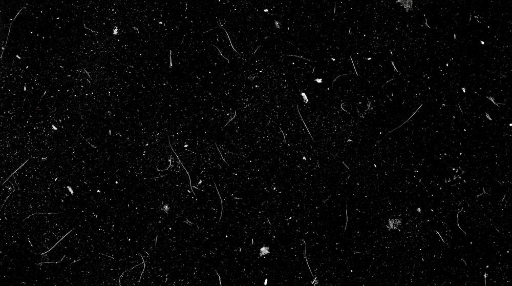 A black background with numerous white analog film dust particles and thin, curved scratches.