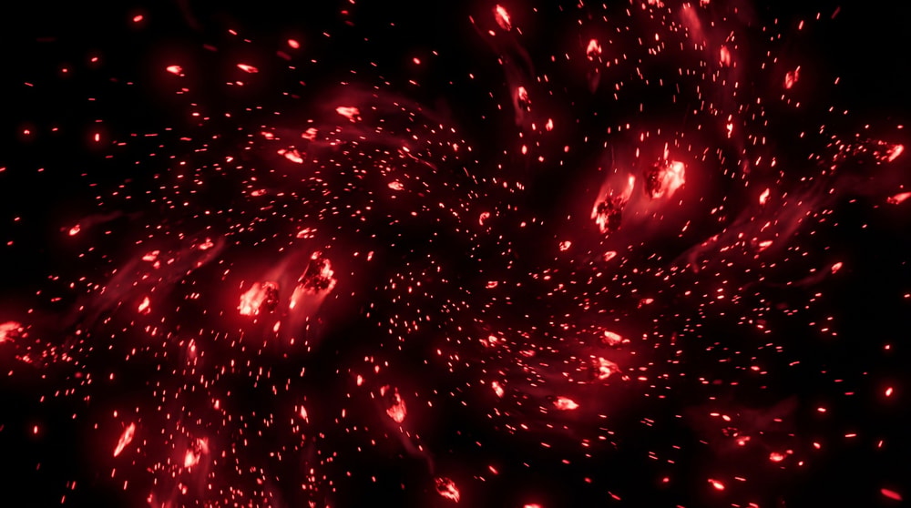 Abstract visualization of numerous small, glowing red embers scattered and swirling against a dark, cosmic background.