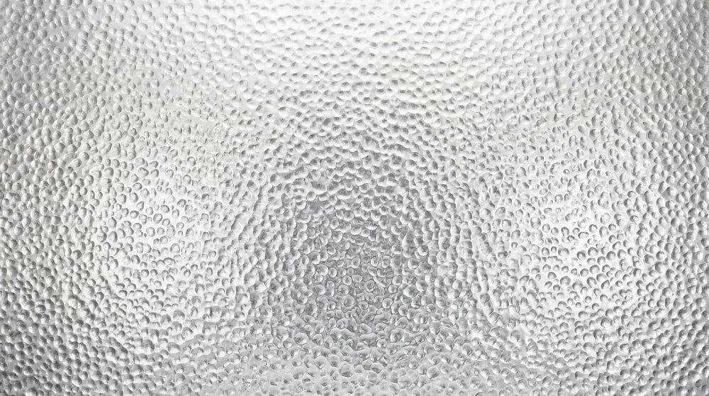Close-up view of a high-resolution metallic surface featuring a repetitive hammered, dimpled texture pattern in a uniform silver-grey finish.