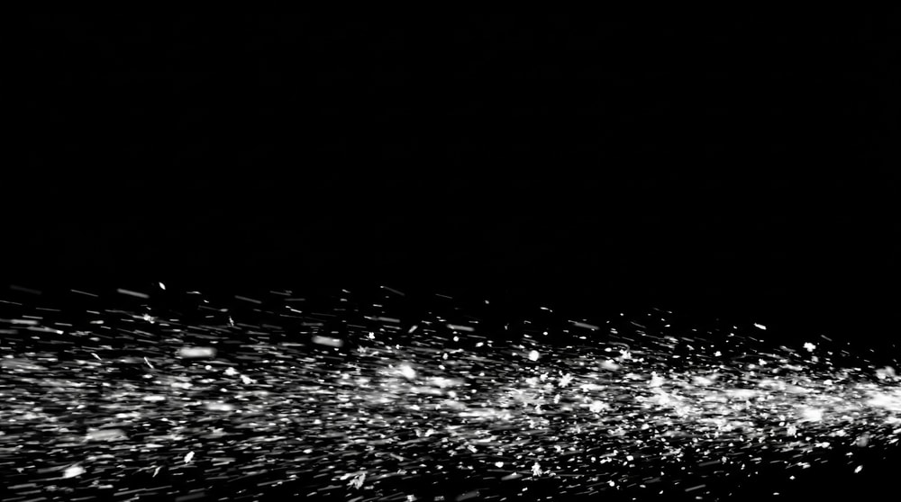 A dynamic spray of fine snow particles moving horizontally across a black background.
