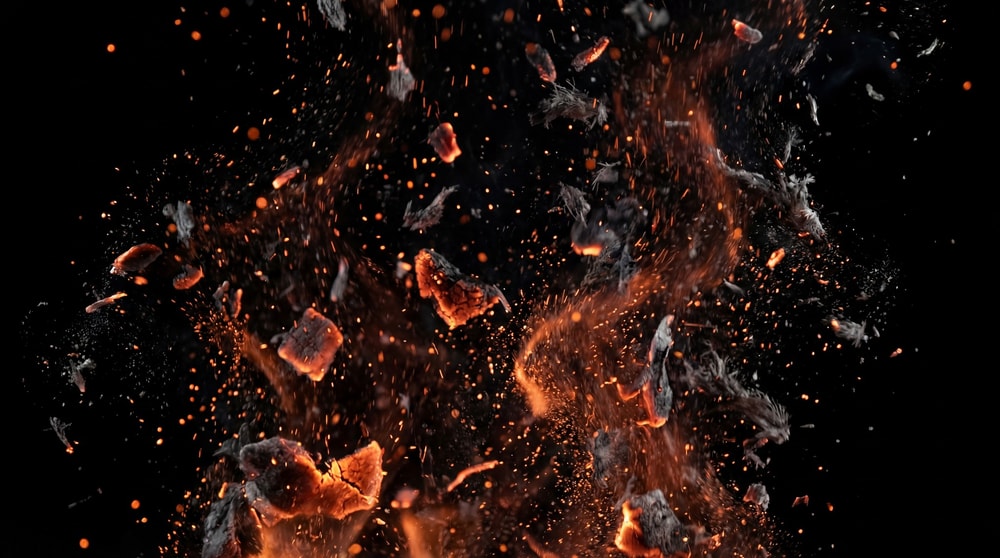 Explosion of glowing orange embers and dark smoke particles against a black background.