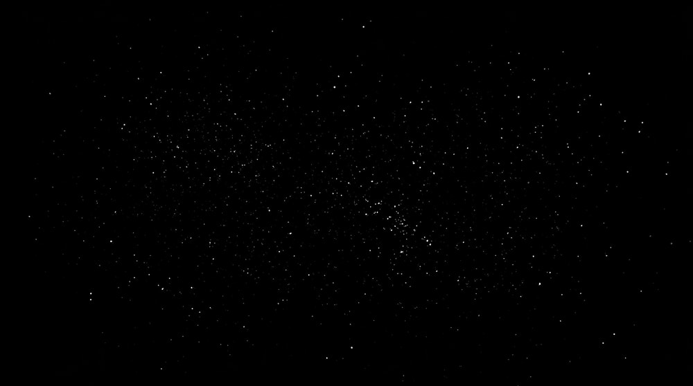 A black background covered in a dense, monochromatic scattering of fine, white dust-like particles resembling subtle film grain.