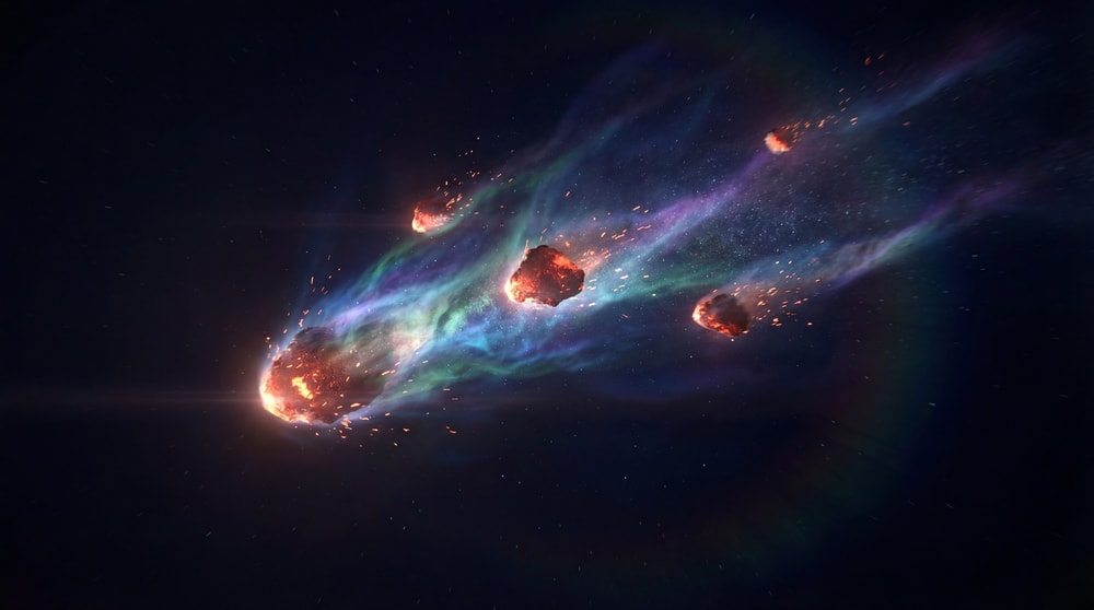 A large, fiery asteroid fragmenting and trailing colorful nebulae and smaller debris across a dark, star-filled expanse.