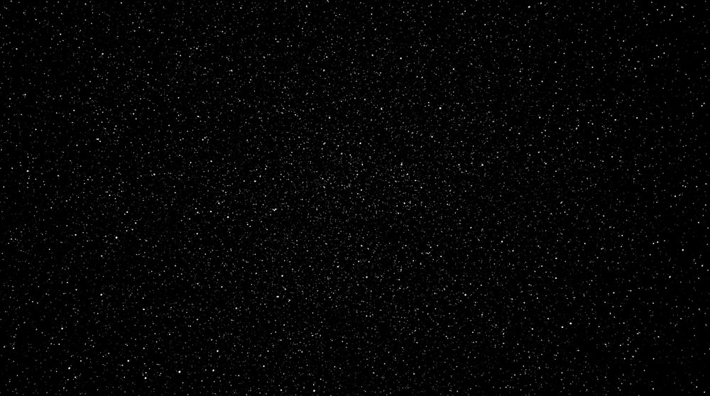 A black background filled with a dense, subtle pattern of fine white specks resembling monochromatic film grain.