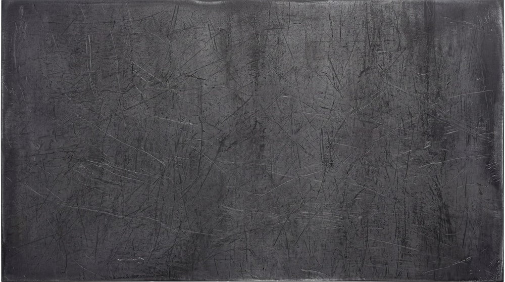 A dark, raw steel surface featuring heavy linear scratches and industrial wear across the entire metallic texture.