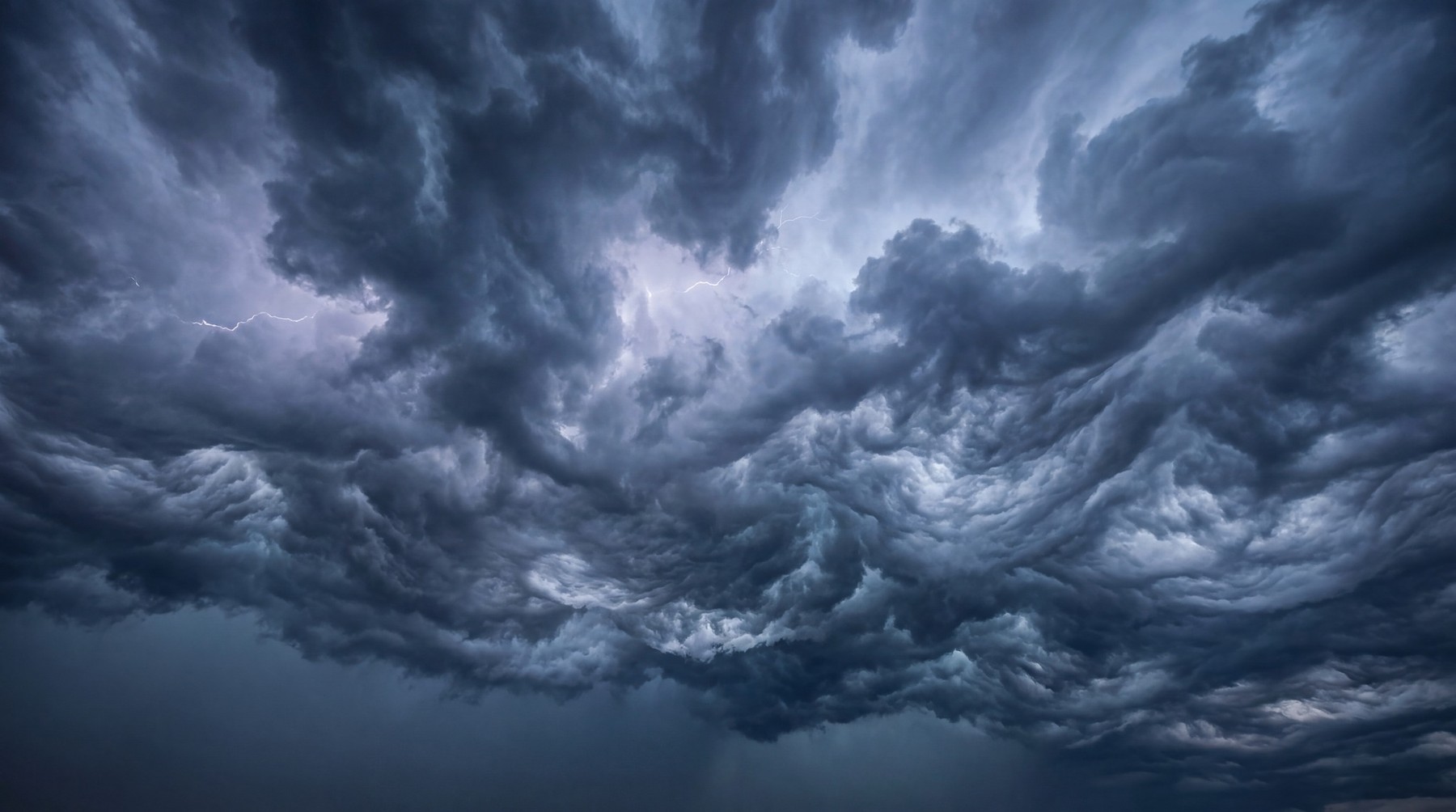 A dramatic and foreboding sky filled with dark, turbulent storm clouds, with faint lightning visible.