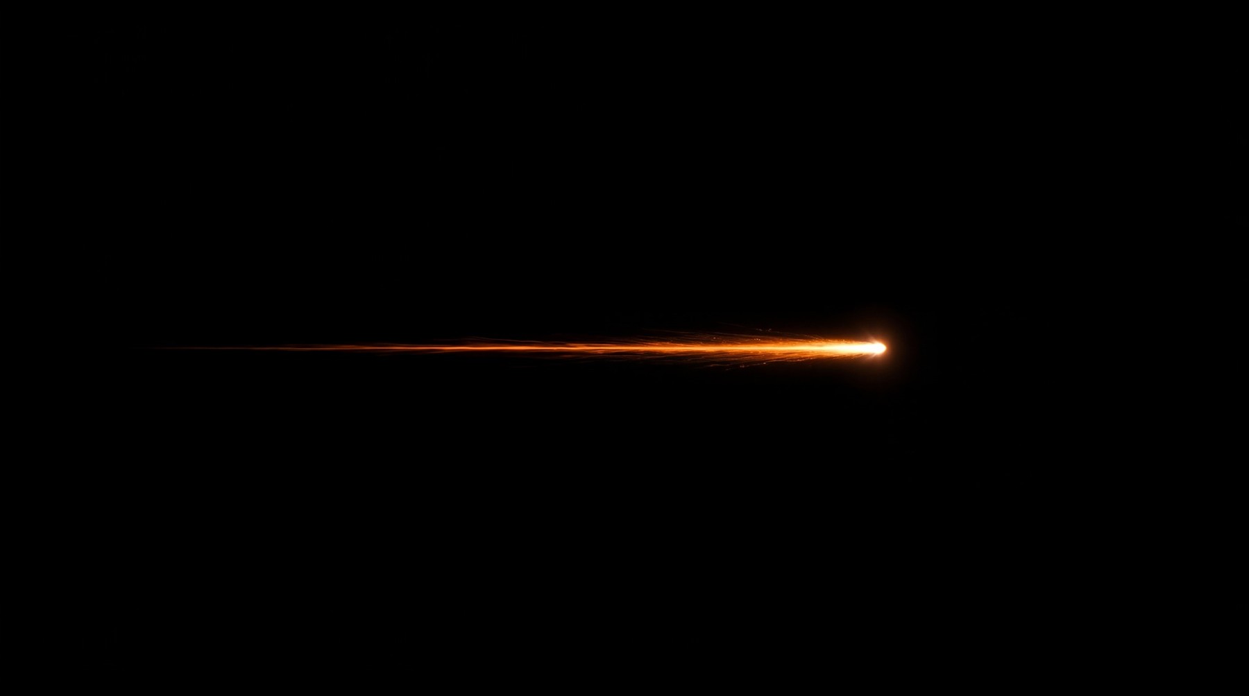 A single, thin shooting star with a bright orange core and a faint, fragmented trail moving horizontally from left to right against a black background.
