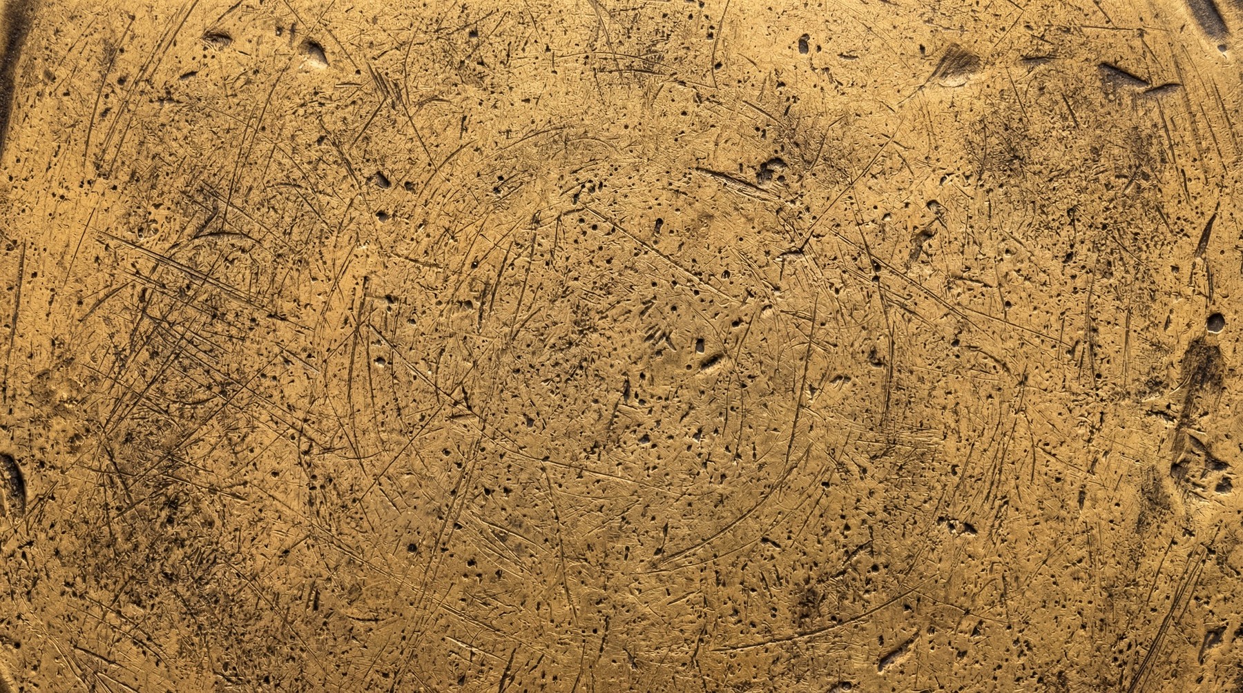 Close-up of a textured gold surface with numerous fine scratches and pitting.