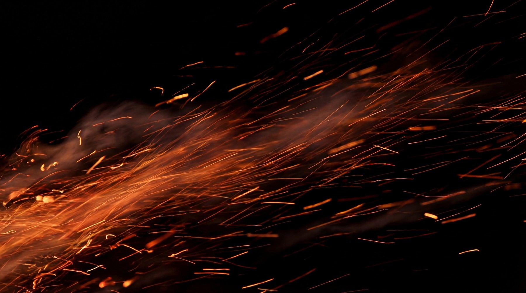Glowing orange fire sparks and heat embers streaking across a deep black background