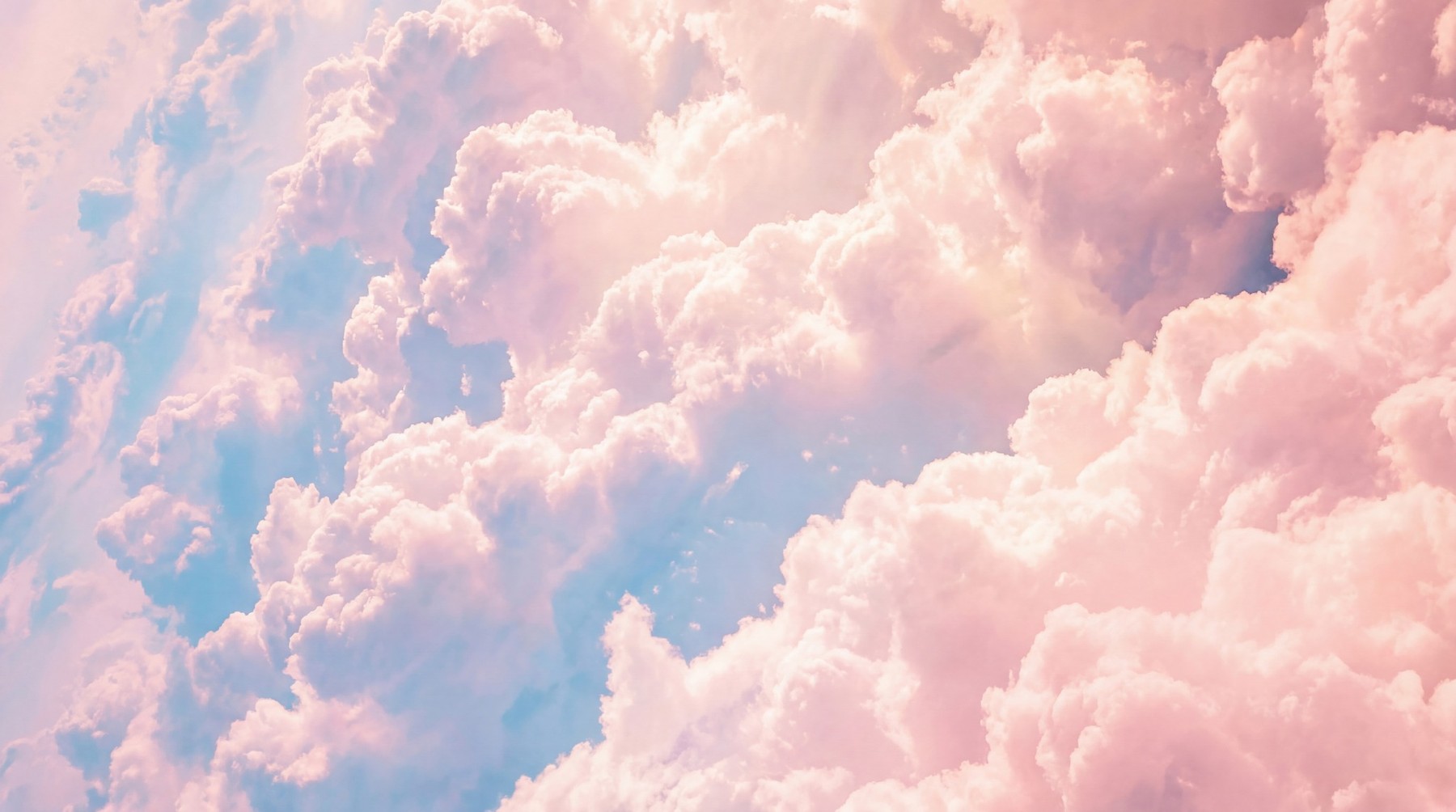 Close-up view of dense, fluffy cumulonimbus clouds with a soft pink and light blue color gradient, illuminated by gentle sunlight.