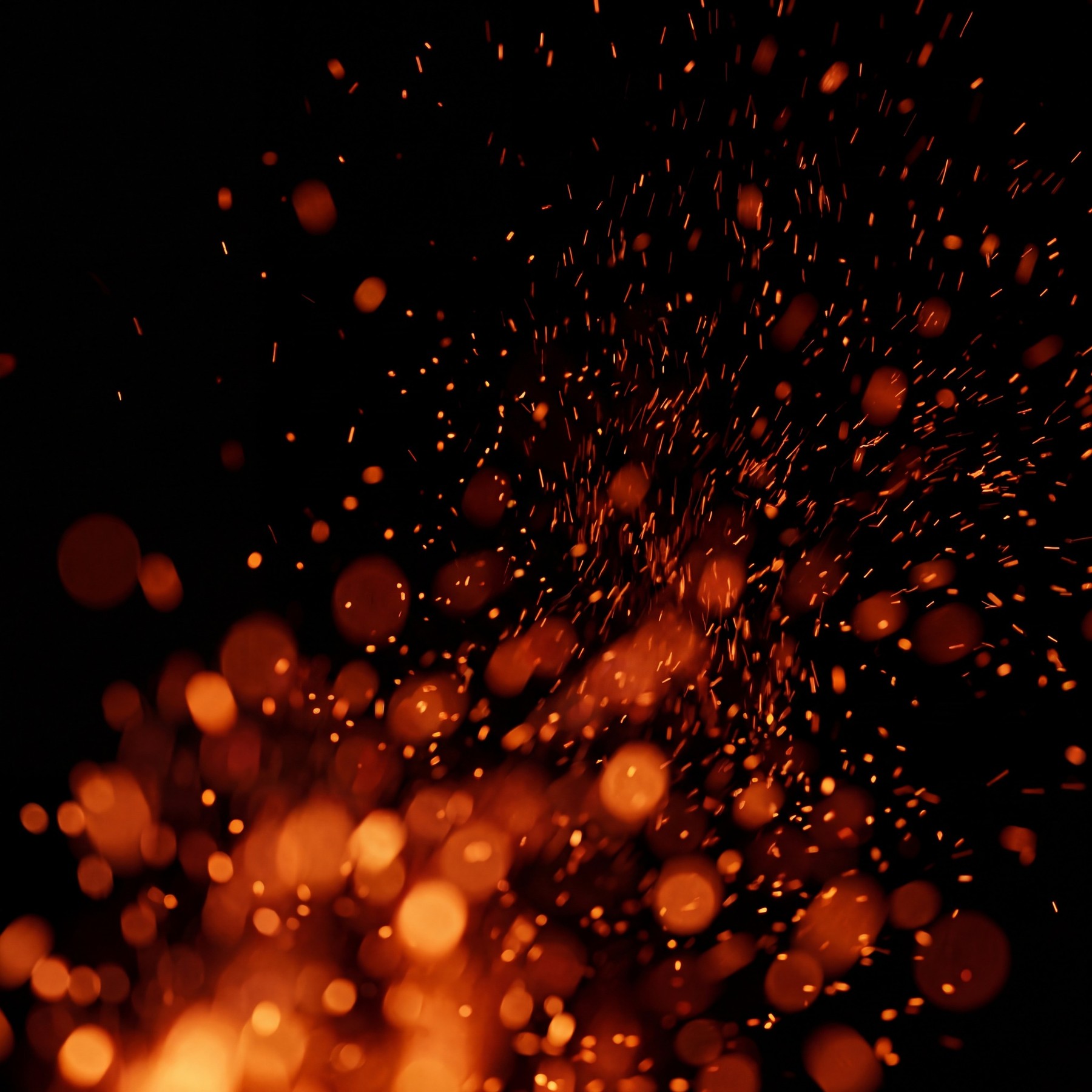 Fiery embers and glowing orange bokeh particles scattered against a black background.