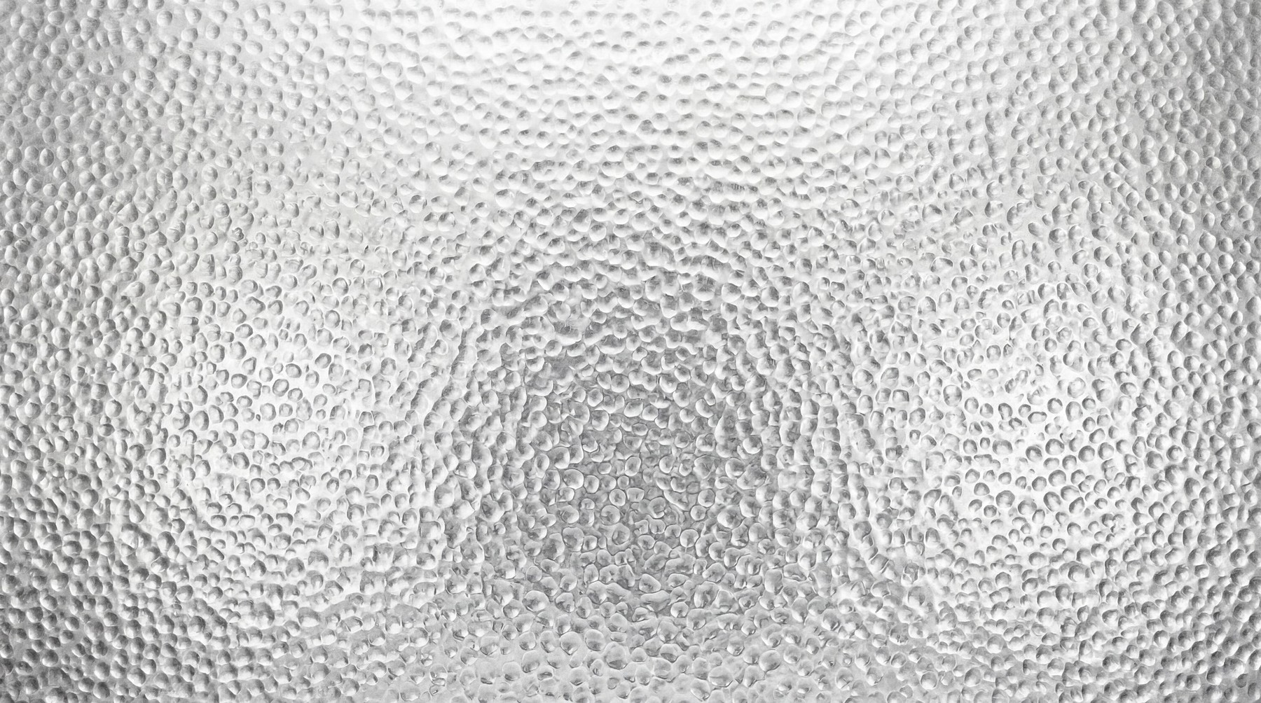 Close-up view of a high-resolution metallic surface featuring a repetitive hammered, dimpled texture pattern in a uniform silver-grey finish.