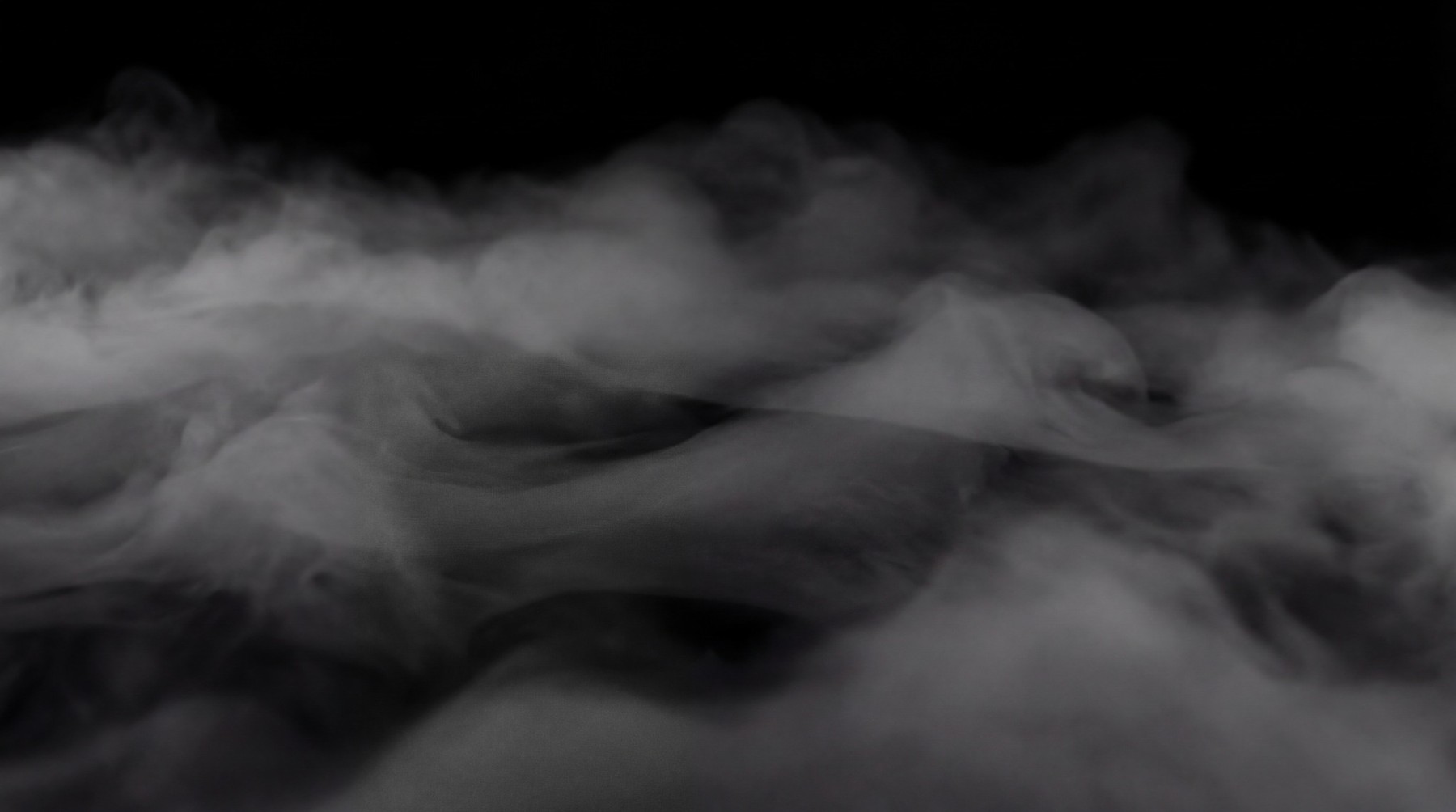 A low-lying, dense layer of white fog covers the bottom half of the frame against a black background, with visible swirling patterns and subtle textures.
