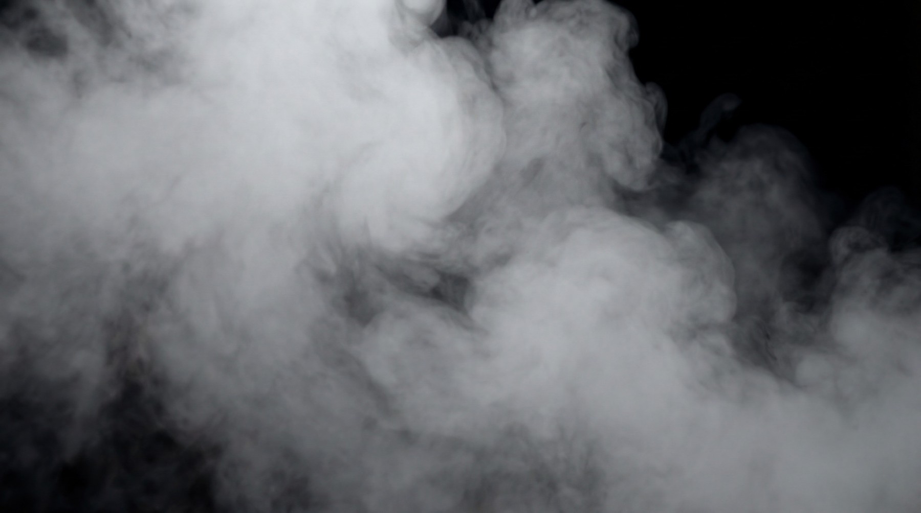 A dense blast of swirling fog and mist against a black background, appearing thick and volumetric.