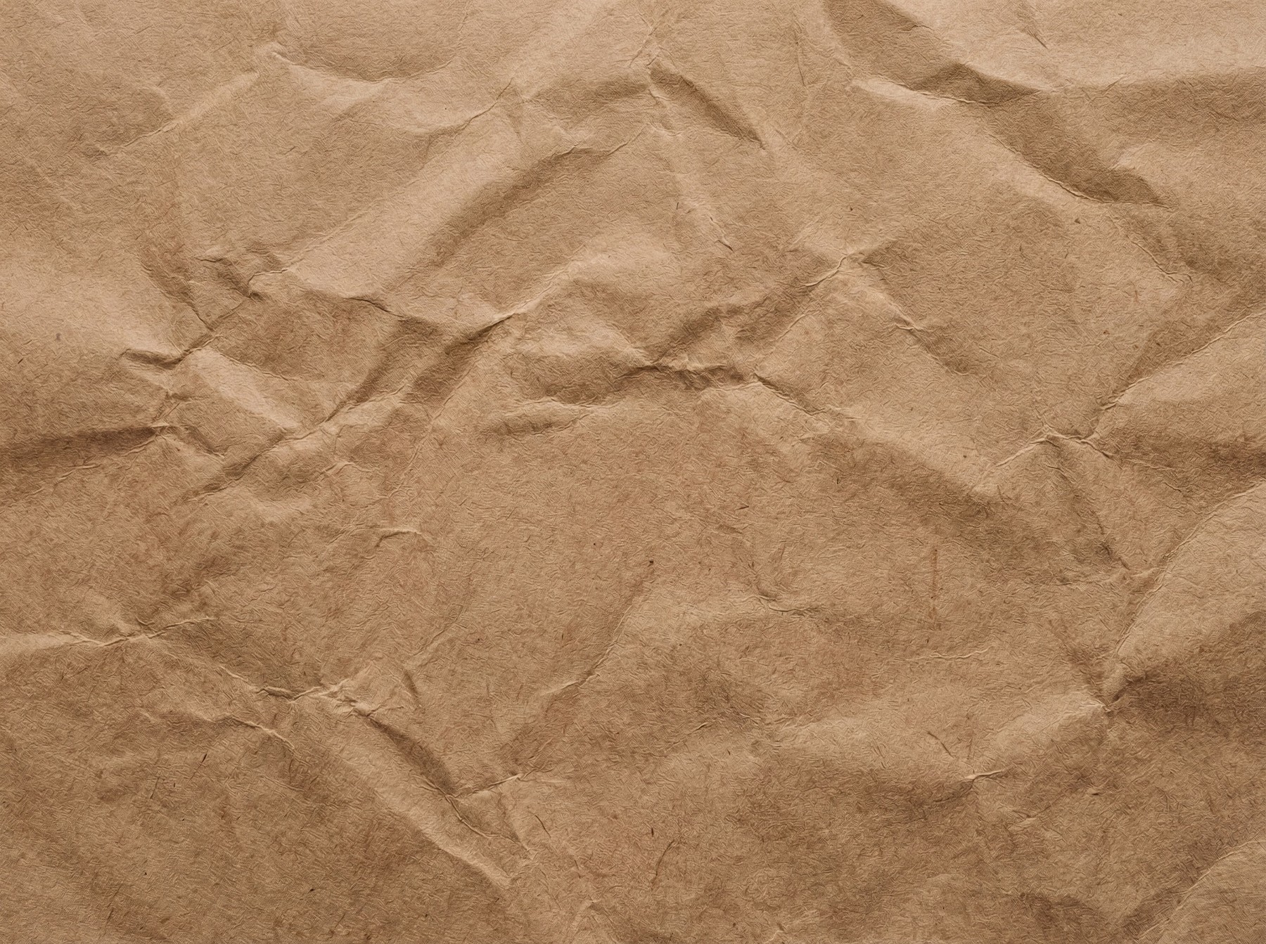 A close-up, top-down view of a crumpled sheet of light brown kraft paper, showing prominent wrinkles and folds.