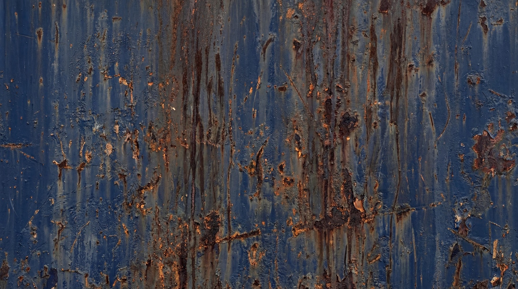 A close-up view of navy blue painted steel featuring heavy rust streaks, paint peeling, and scattered surface scratches.