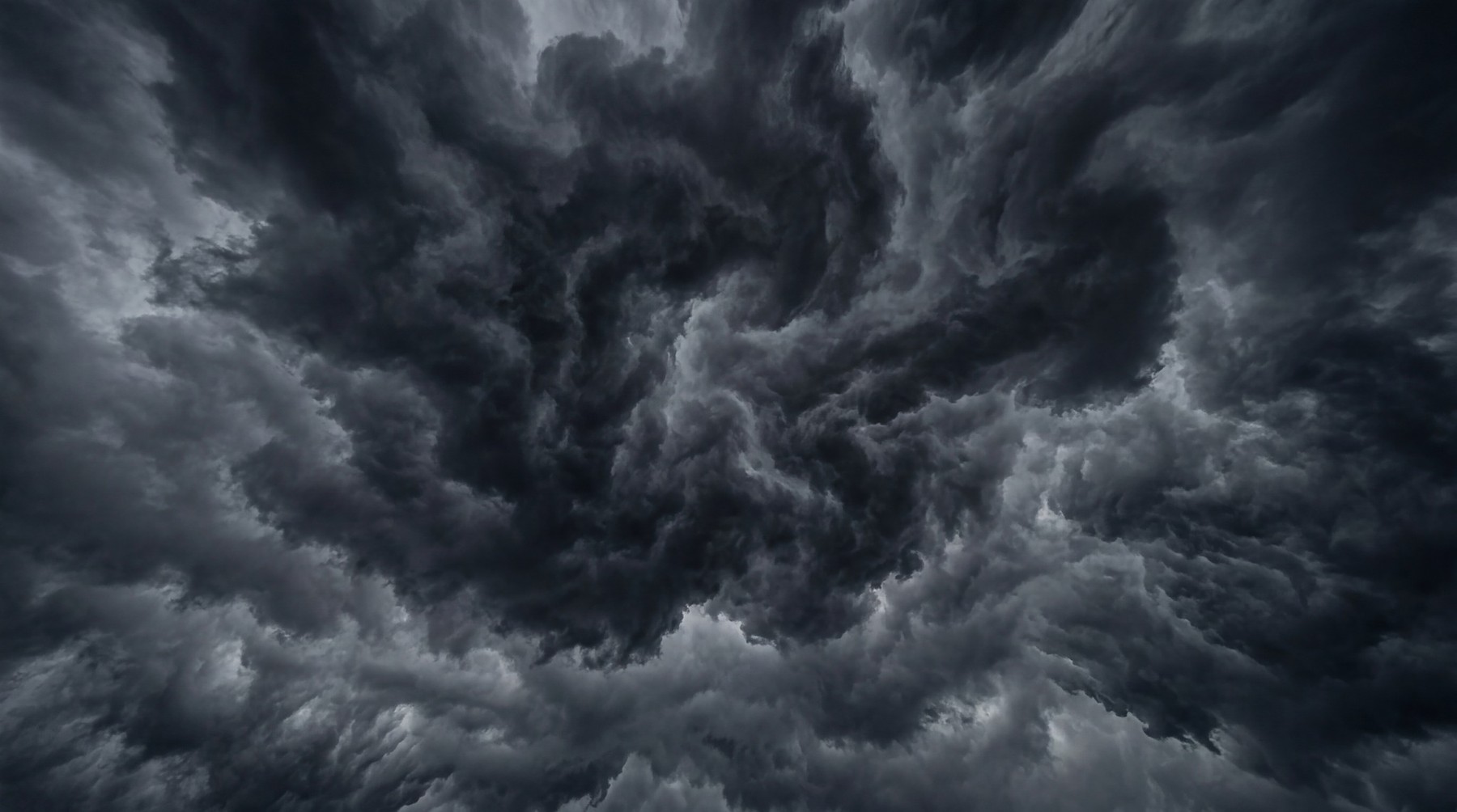 Dramatic dark grey and black swirling storm clouds viewed from below.