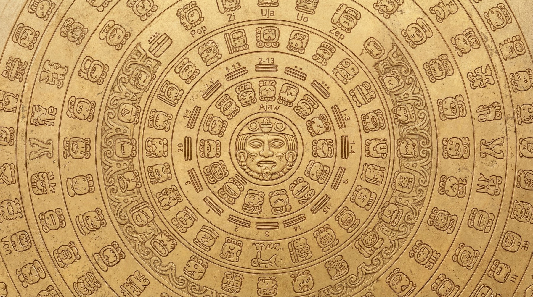 Close-up of an ornate, circular Mayan calendar carved into a textured gold surface, featuring glyphs and numerical elements.
