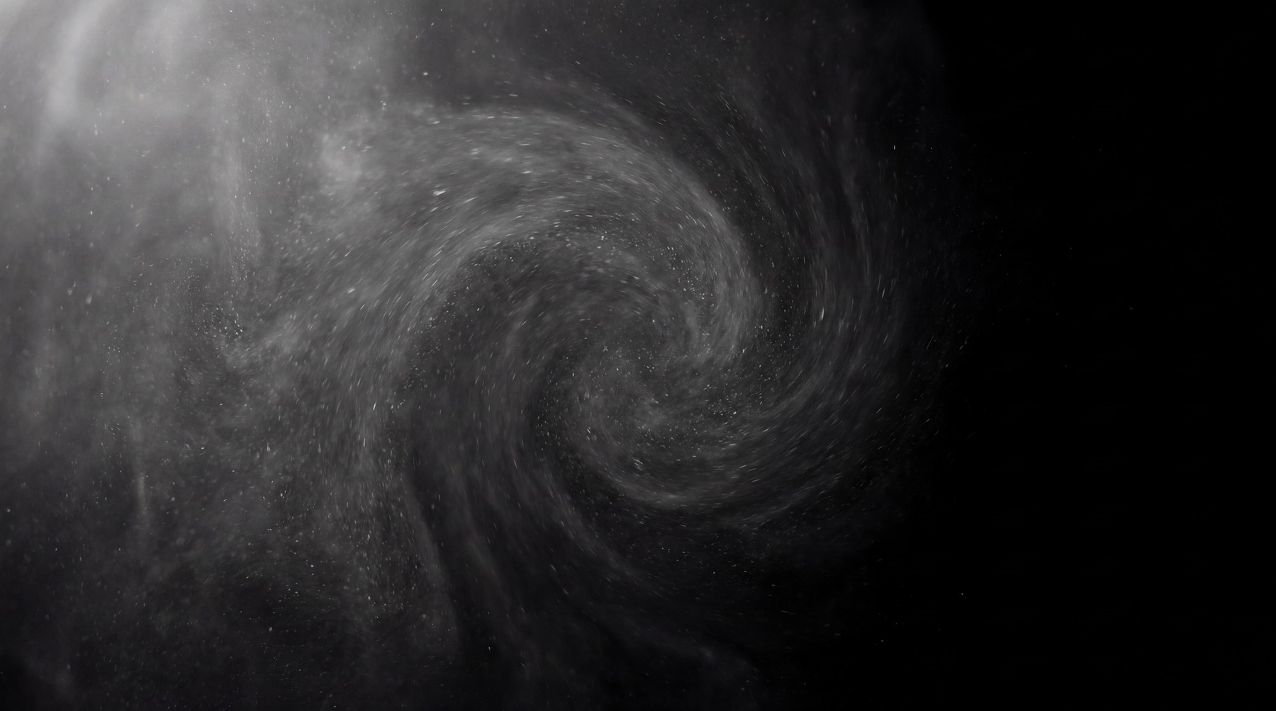 A dynamic vortex of fine white dust particles swirling against a stark black background.