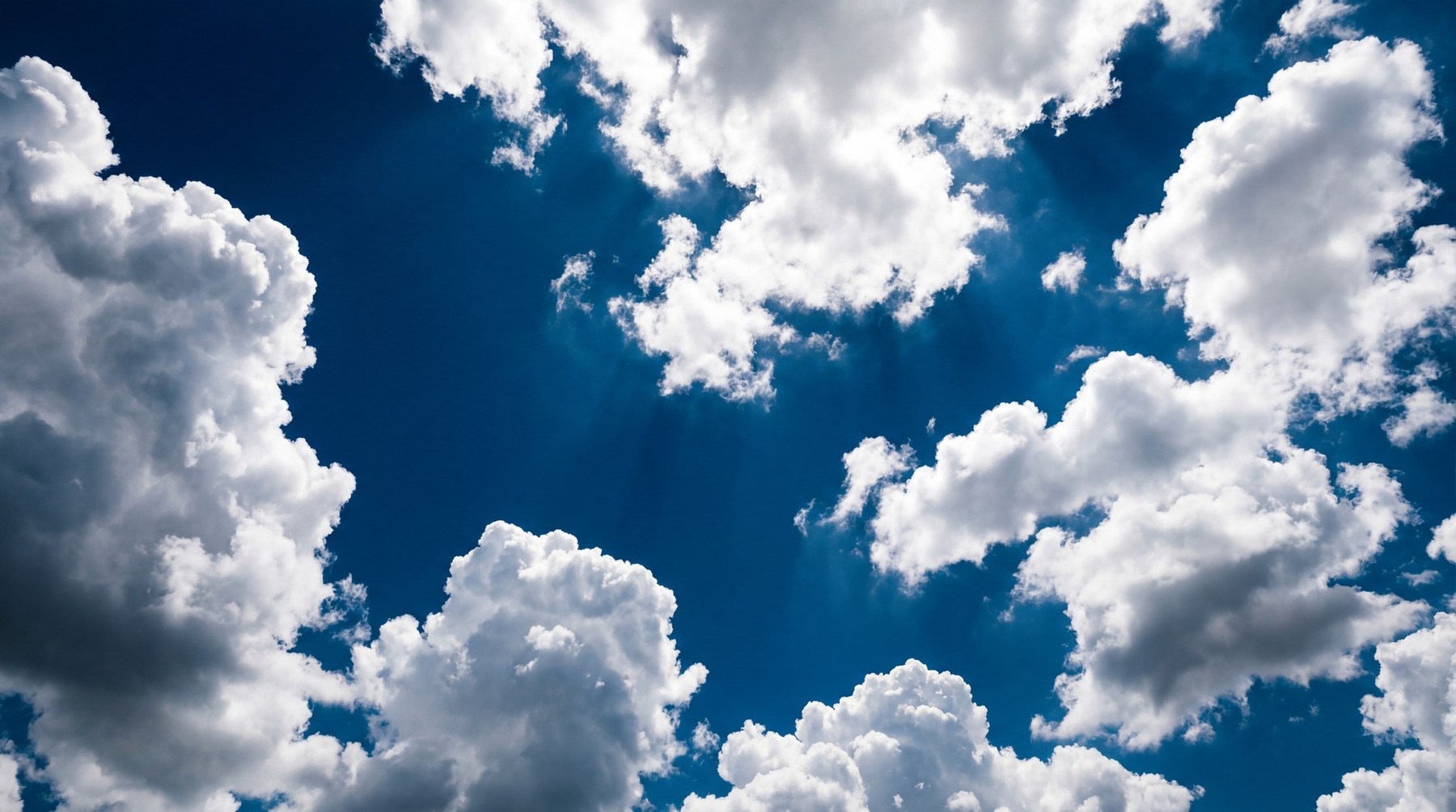 A clear, deep blue sky filled with voluminous white cumulus clouds, illuminated by bright sunlight from above.