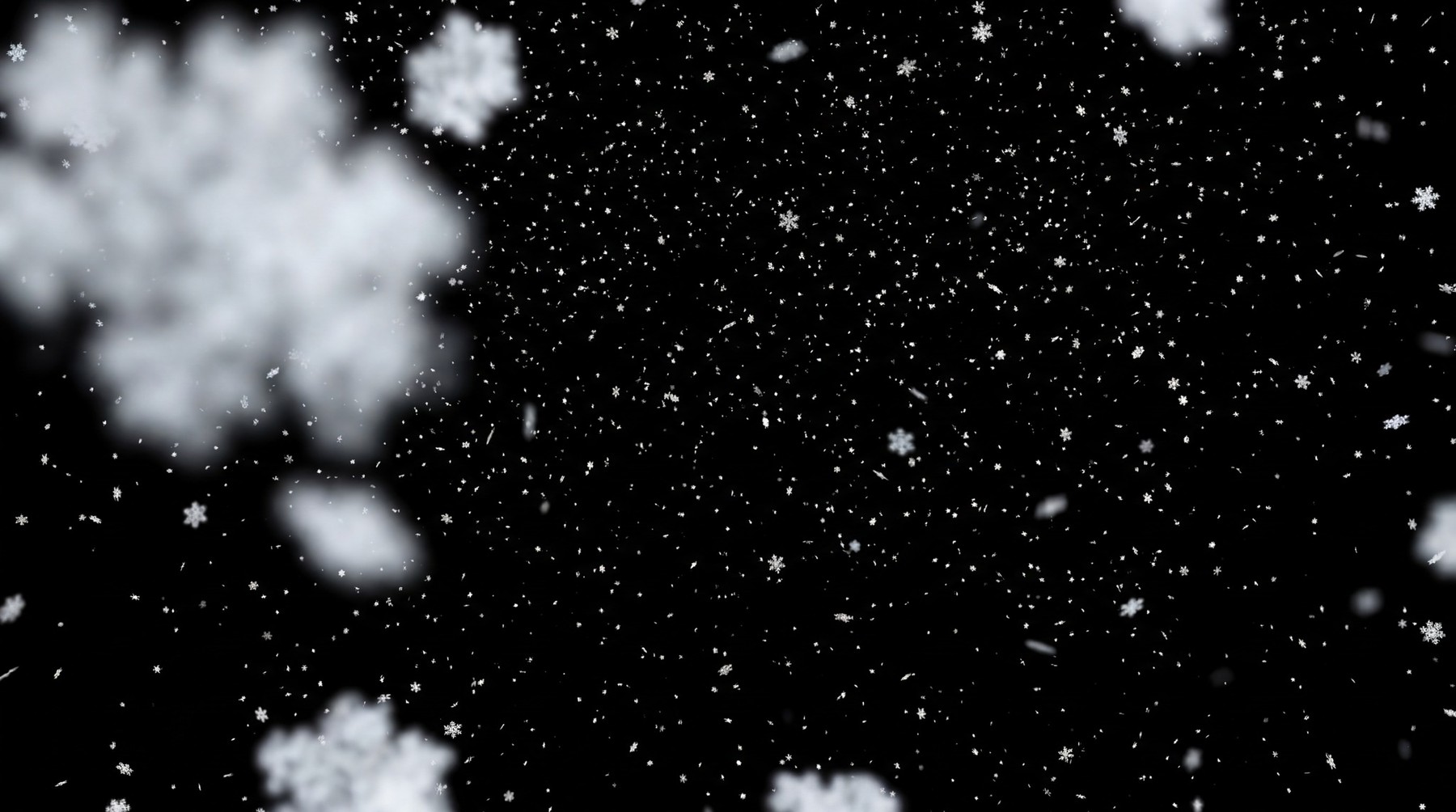 Moderate snowfall with large, detailed snowflakes in the foreground and smaller, scattered flakes throughout the frame against a black background.