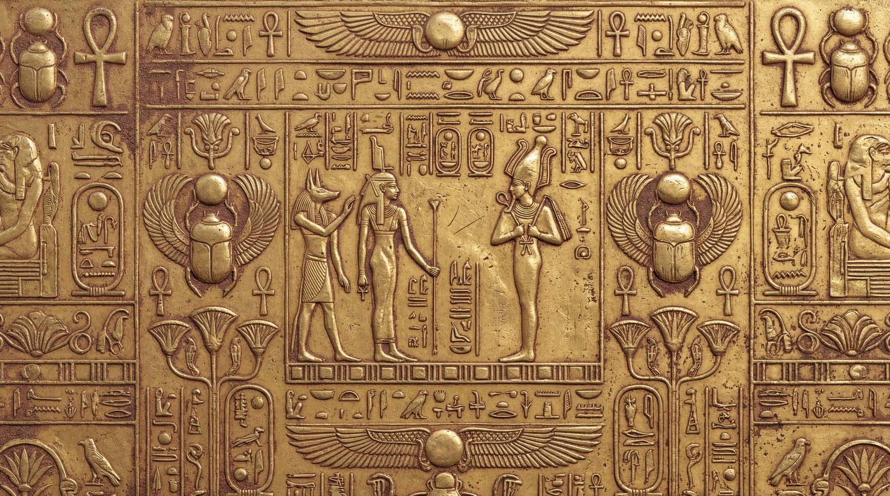 Close up of a metallic gold surface embossed with ancient Egyptian deities and hieroglyphics in a bas-relief style.