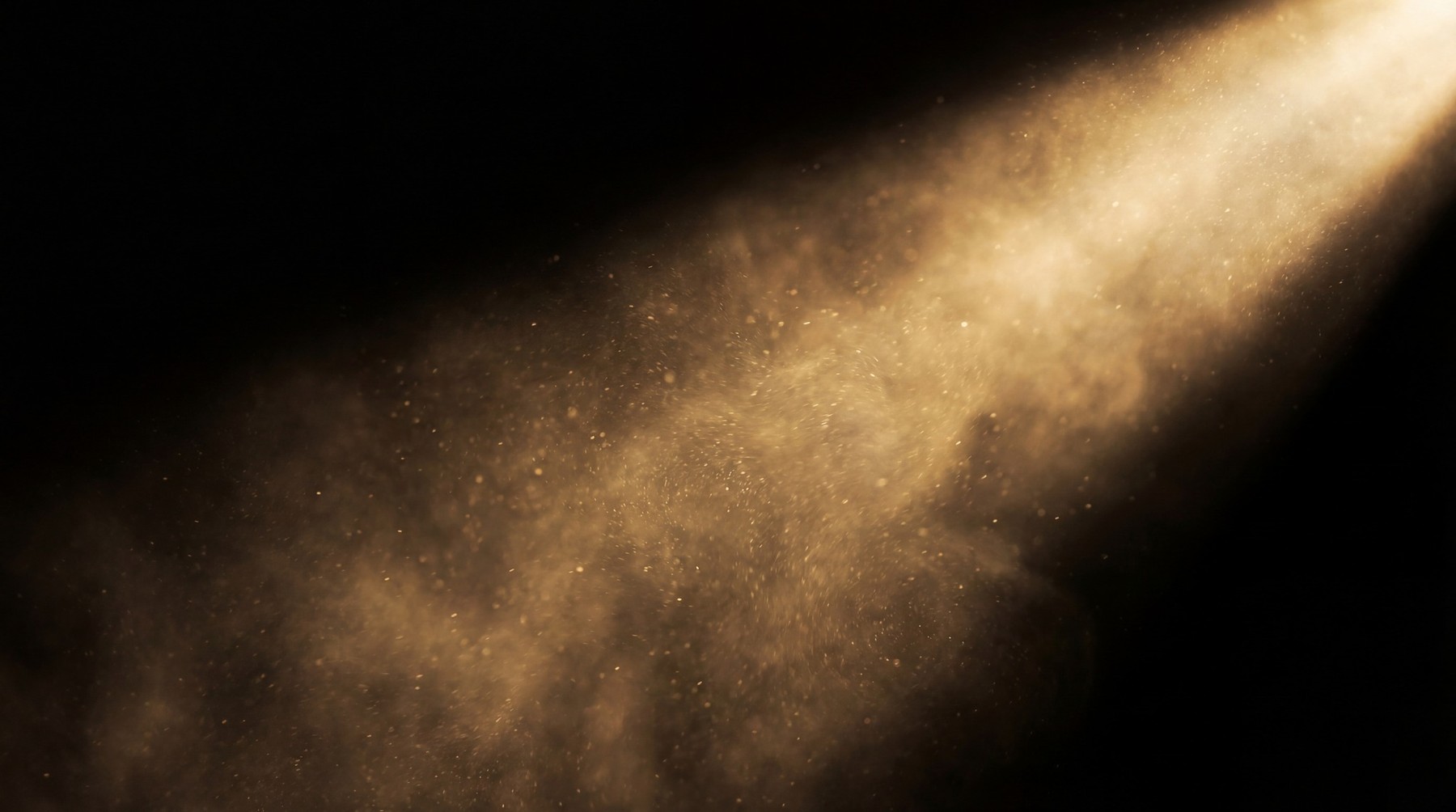 A dramatic spotlight illuminates a dense haze of golden particles against a black background.