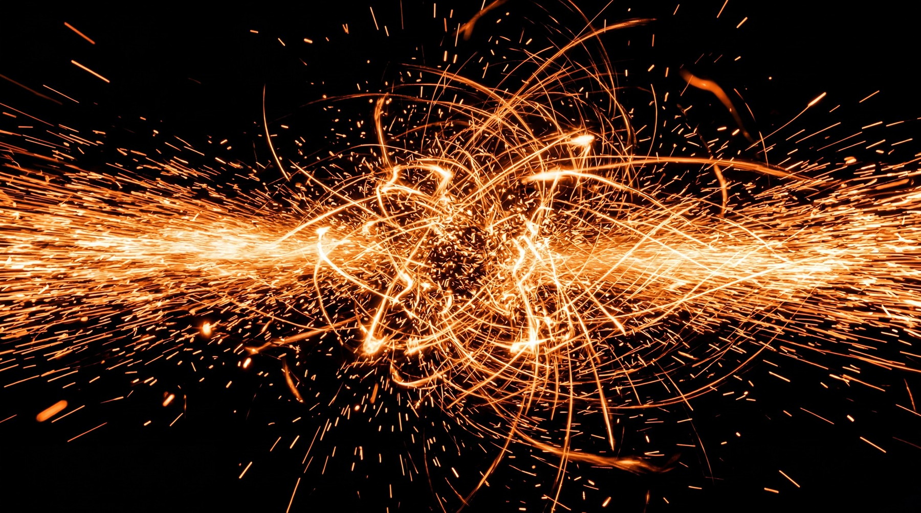 Abstract composition of vibrant orange spark trails and glowing embers against a black background.