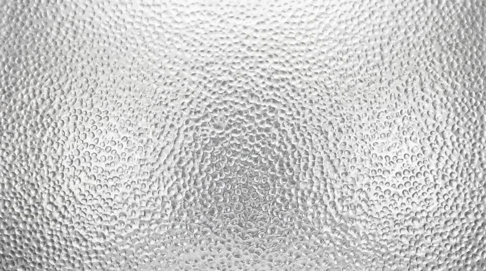 Close-up view of a high-resolution metallic surface featuring a repetitive hammered, dimpled texture pattern in a uniform silver-grey finish.