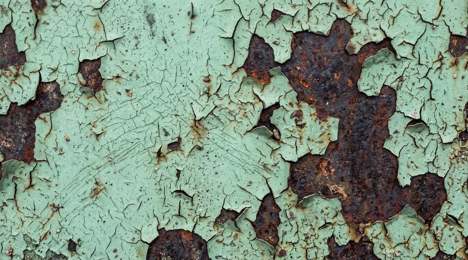 High-resolution texture of peeling mint green paint revealing dark rusted metal beneath.