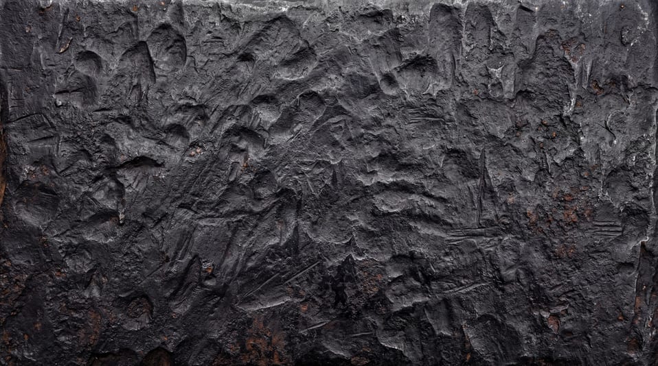 A close-up of a raw forged steel surface featuring deep impact marks, heavy indentations, and coarse dark grey metal pitting.