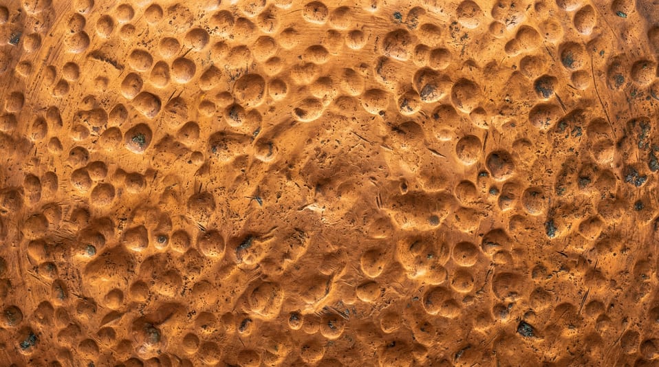 Close-up of a rustic hammered copper metal sheet with visible circular indentations and natural surface weathering.