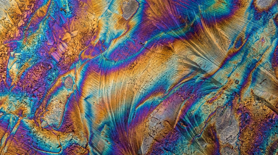 Close-up view of heat-treated steel showing vibrant iridescent temper colors with blue, purple, and gold swirling patterns.